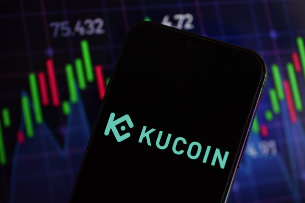 Kucoin logo on iPhone display screen and crypto currency value charts