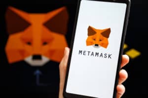 Hand holding mobile with MetaMask app running at smartphone screen with MetaMask and Binance logo at background.