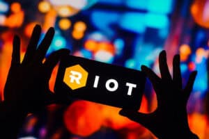 Riot Blockchain Inc. logo is displayed on a smartphone screen.