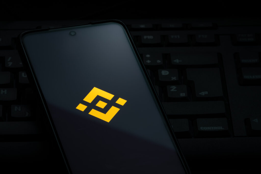 Binance exchange logo on smartphone screen laying on computer keyboard