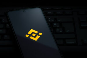 Binance exchange logo on smartphone screen laying on computer keyboard