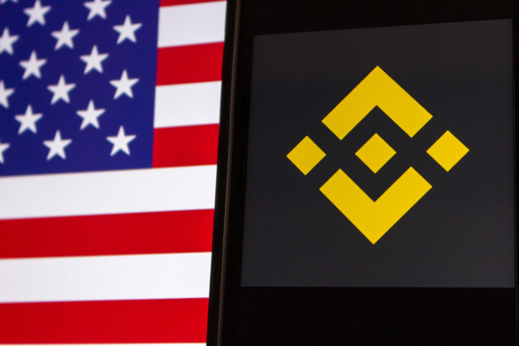 Binance logo seen in iPhone screen on US flag background.
