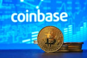 Coinbase logo on a computer screen with a stack of crypto coins