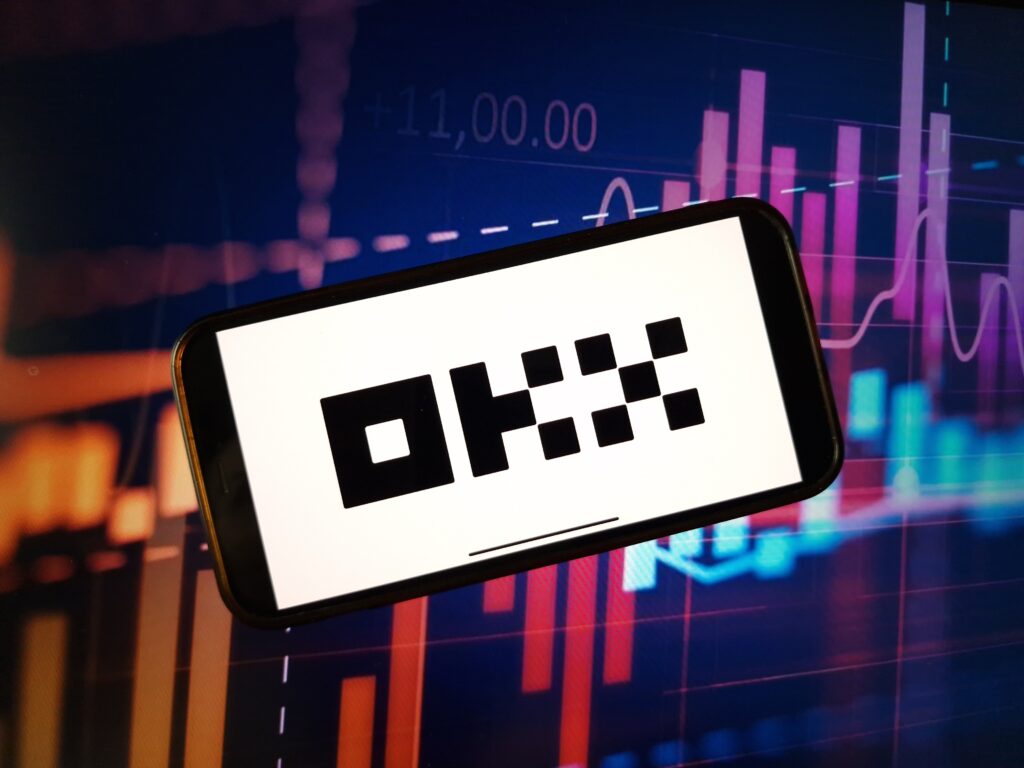 OKX cryptocurrency exchange logo displayed on smartphone on crypto market data background