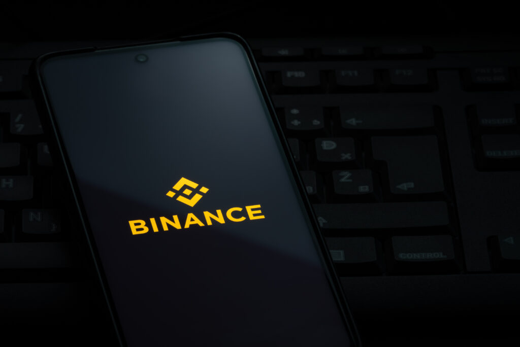 Binance exchange logo on smartphone screen laying on computer keyboard