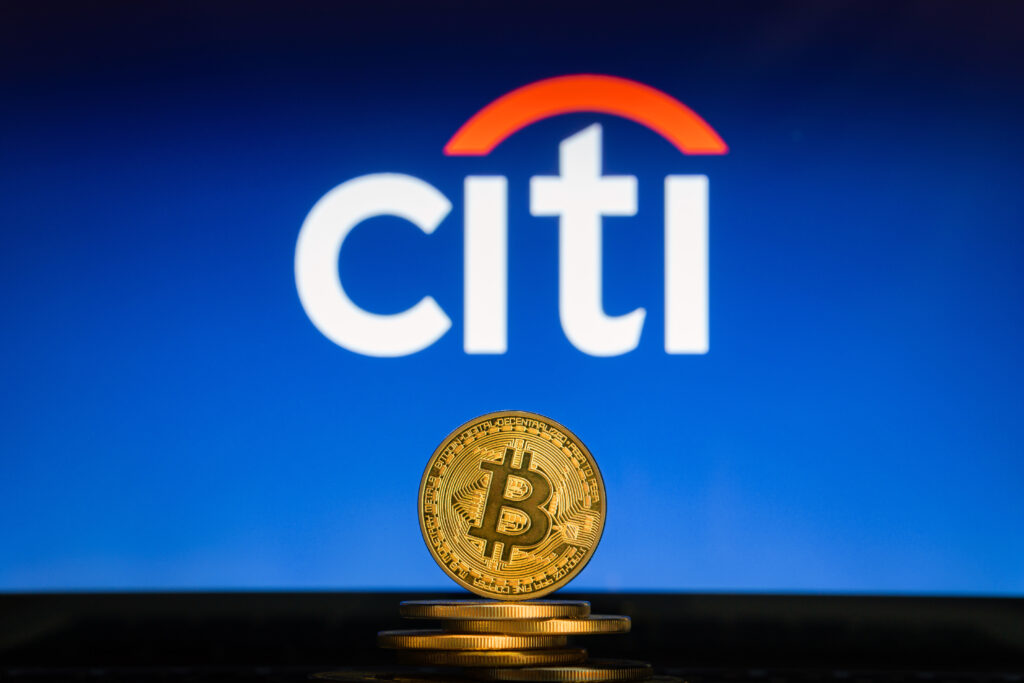 Bitcoin on a stack of coins with Citi Bank logo on a laptop screen.