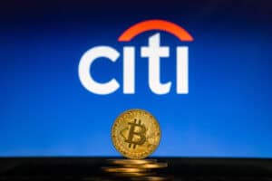 Bitcoin on a stack of coins with Citi Bank logo on a laptop screen.