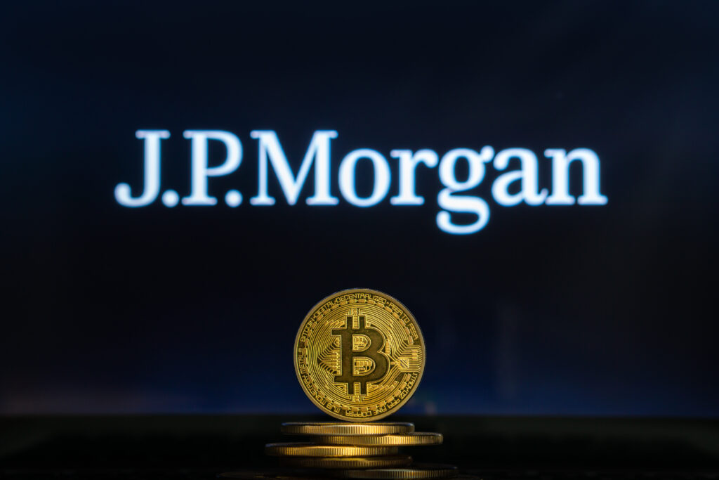 Bitcoin on a stack of coins with JPMorgan logo on a laptop screen.