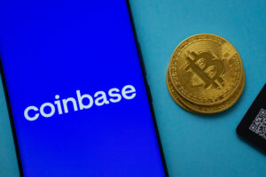 Coinbase logo on smartphone screen near Bitcoin coin and QR code on blue background.