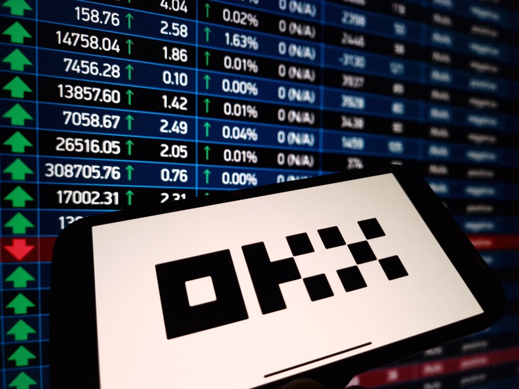 OKX cryptocurrency exchange logo displayed on smartphone on crypto market data background