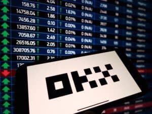 OKX cryptocurrency exchange logo displayed on smartphone on crypto market data background