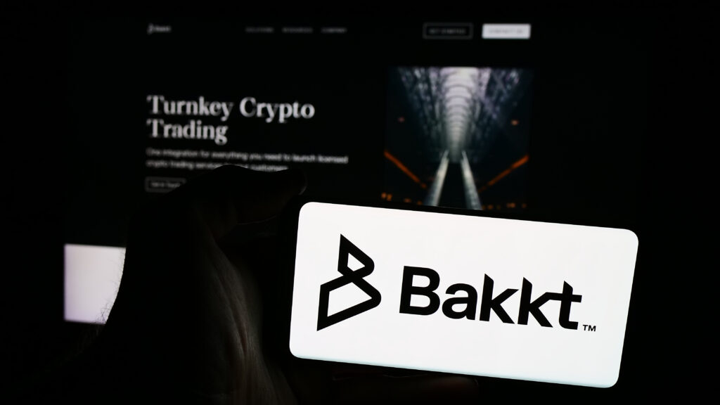 Person holding cellphone with logo of US crypto trading company Bakkt Holdings Inc. in front of business webpage. Focus on phone display.