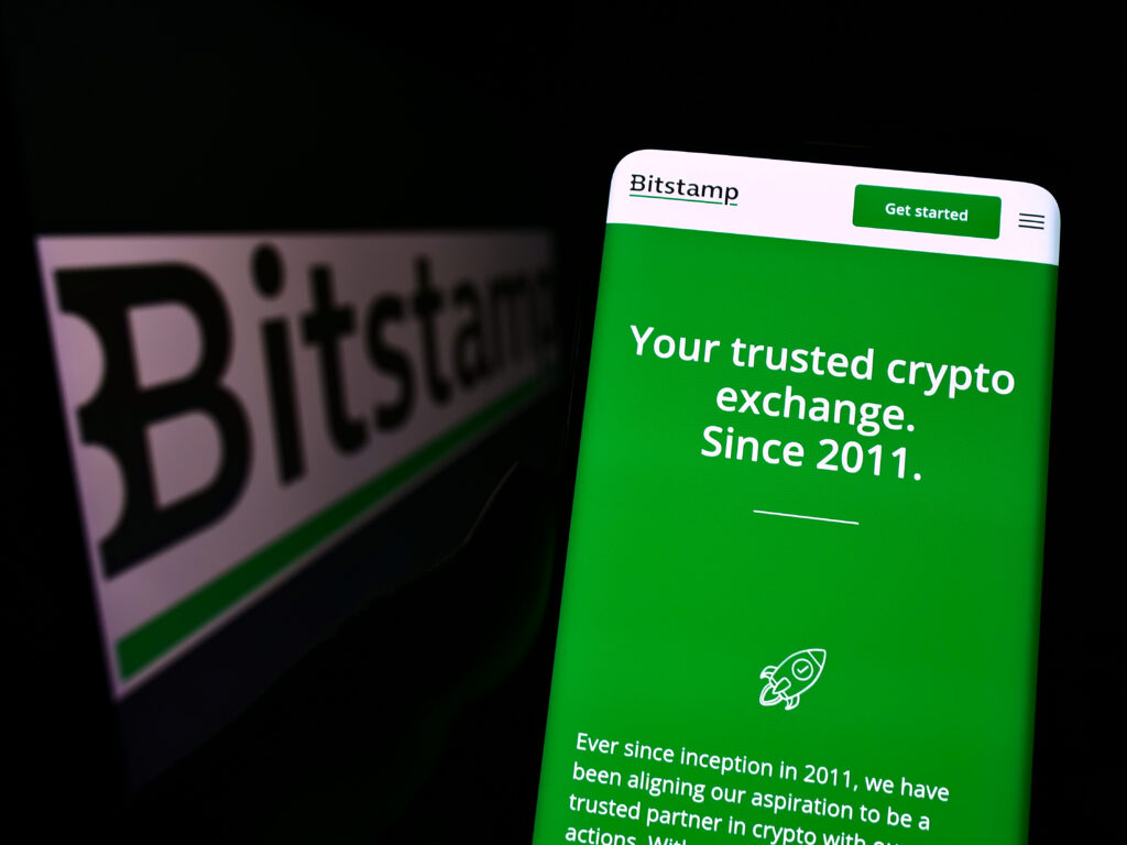 Person holding cellphone with webpage of cryptocurrency exchange company Bitstamp Ltd. on screen with logo. Focus on center of phone display.