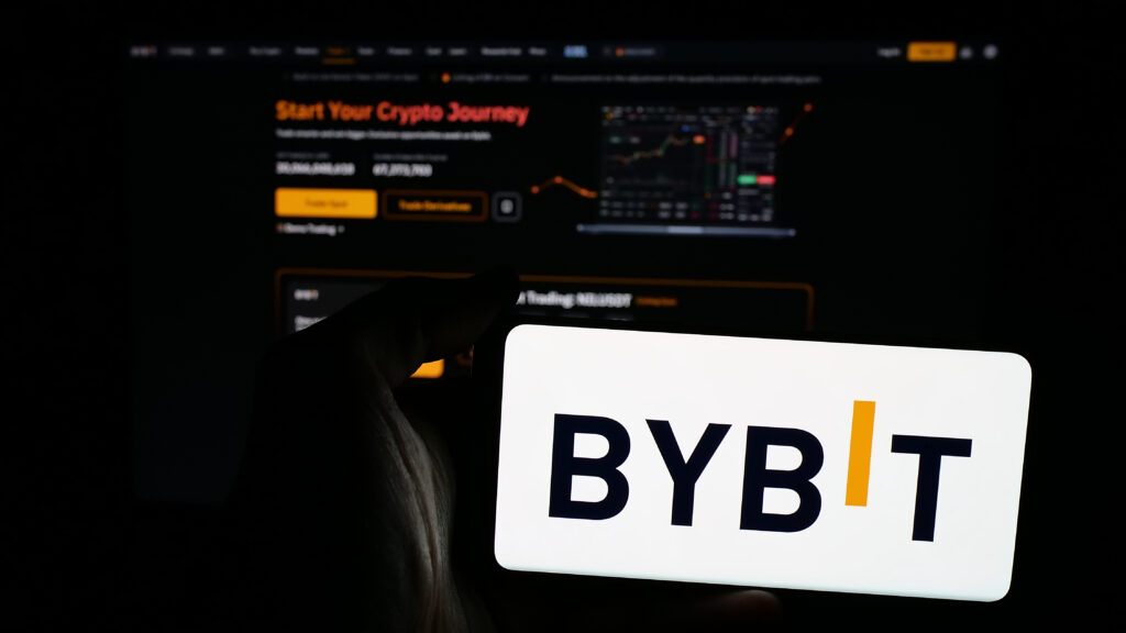 Person holding mobile phone with logo of crypto exchange company Bybit Fintech Limited on screen in front of web page.