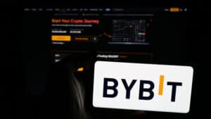 Person holding mobile phone with logo of crypto exchange company Bybit Fintech Limited on screen in front of web page.
