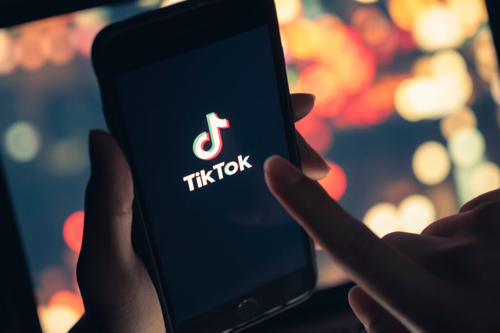 Tik Tok application icon on iPhone 11 pro max screen in hand and have a bokeh for background.