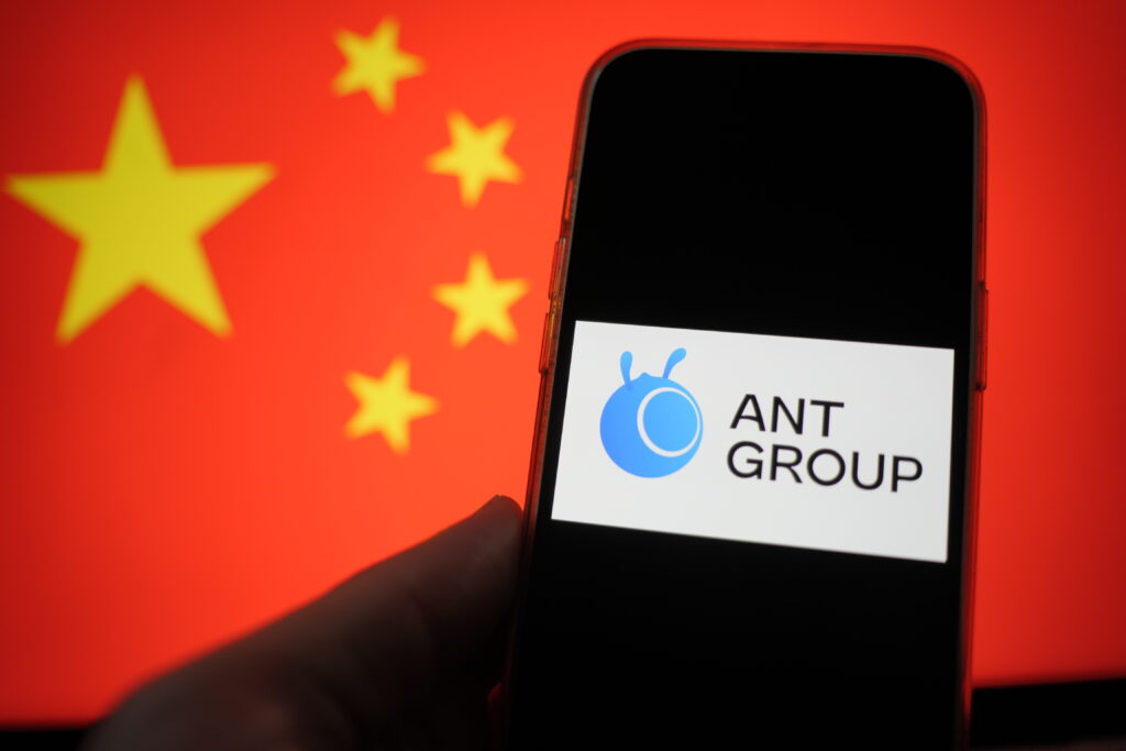 A mobile phone displaying the logo of Ant Group, with the Chinese flag in the background.