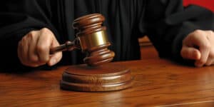 Male judge hand holding striking gavel to bang on sounding block in court room, pronounces verdict, close up detail.