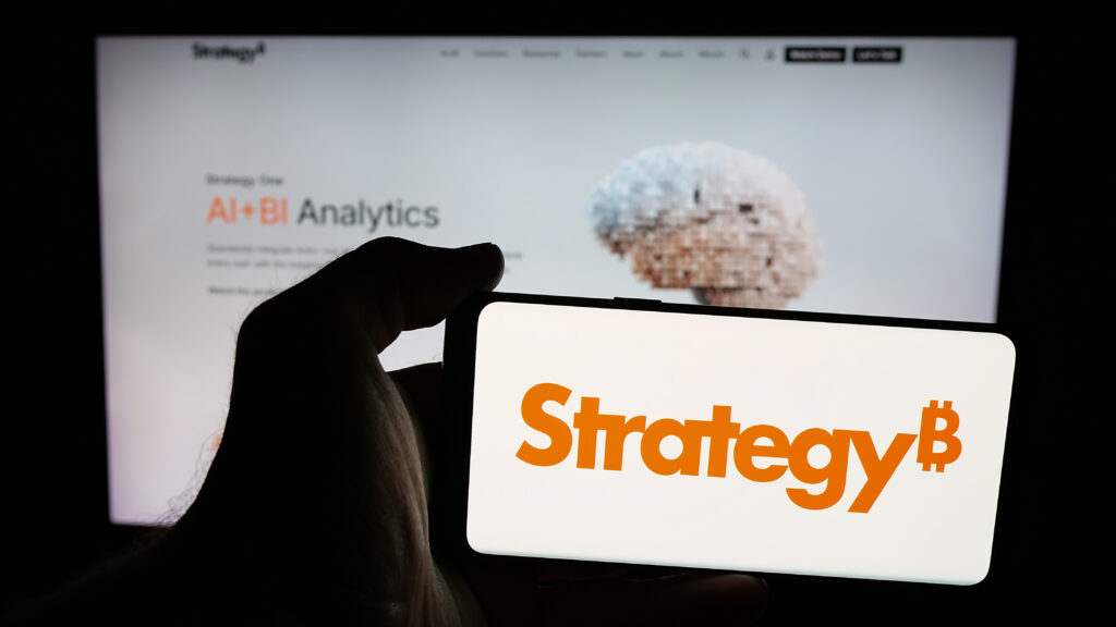 Person holding mobile phone with logo of US company MicroStrategy Inc. on screen in front of web page.