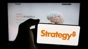 Person holding mobile phone with logo of US company MicroStrategy Inc. on screen in front of web page.
