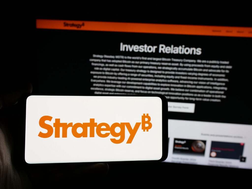 Person holding smartphone with logo of US company MicroStrategy Inc. on screen in front of website.