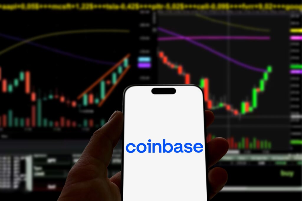 Smartphone with coinbase logo is held in front of a screen that displays stock or cryptocurrency charts, bitcoin, investment, blockchain, trading, growth, success