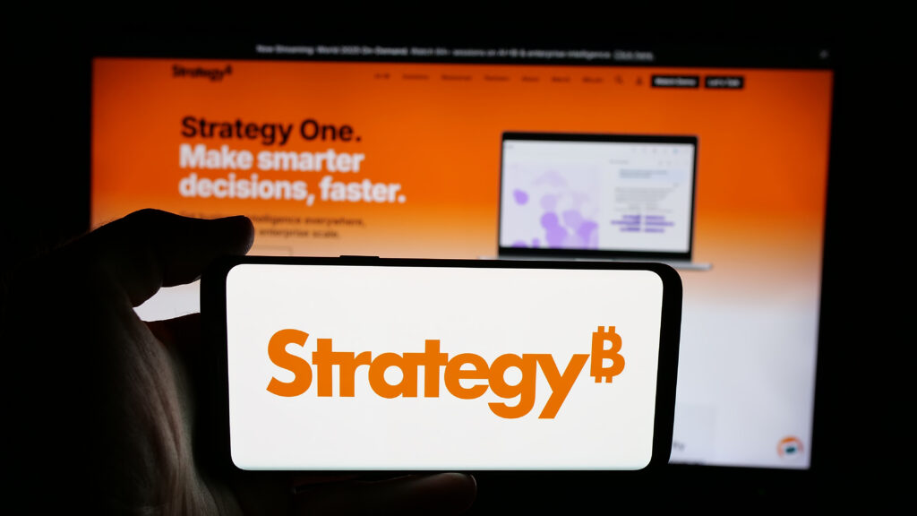 Person holding cellphone with logo of US company MicroStrategy Inc. on screen in front of webpage.