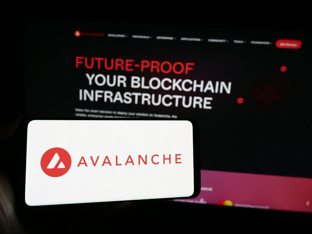 Person holding cellphone with logo of blockchain company Avalanche (BVI) Inc. (Avax Network) in front of webpage.