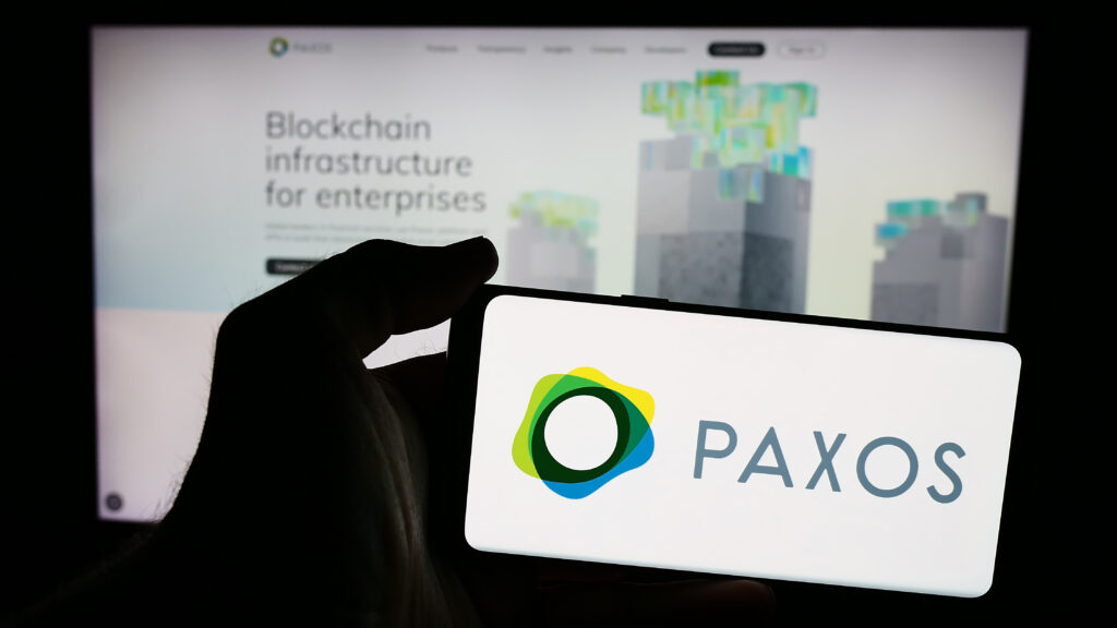 Person holding mobile phone with logo of American blockchain business Paxos Trust Company LLC in front of web page.
