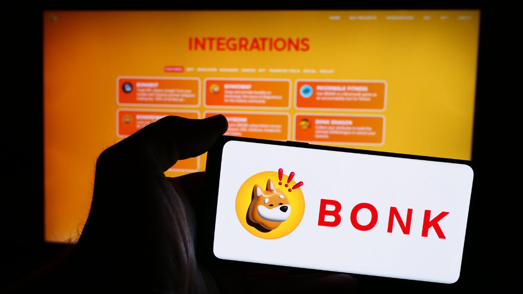 Person holding mobile phone with logo of dog coin company Bonk Inu in front of business web page.