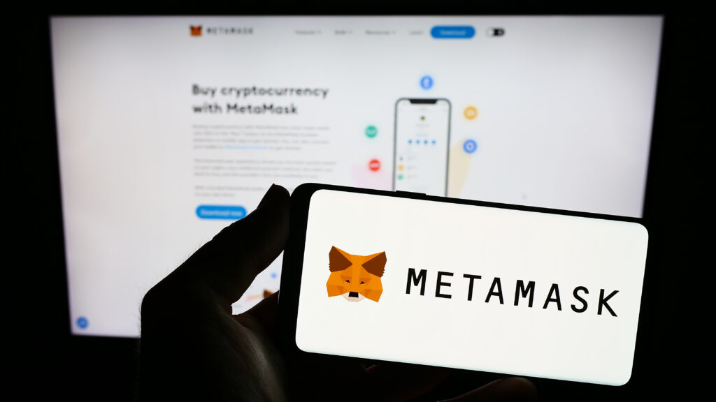 Person holding smartphone with logo of cryptocurrency wallet software MetaMask on screen in front of website.