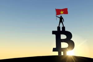 Person waving a vietnam flag standing on top of a bitcoin cryptocurrency symbol.