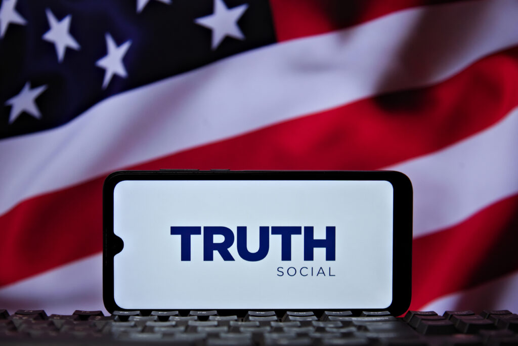 The logo of Truth Social, President Trump's (TMTG) social media platform, is seen on a cell phone screen with the American flag in the background.