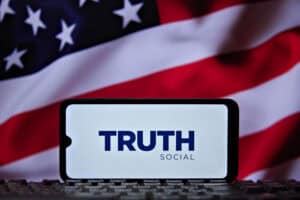 The logo of Truth Social, President Trump's (TMTG) social media platform, is seen on a cell phone screen with the American flag in the background.