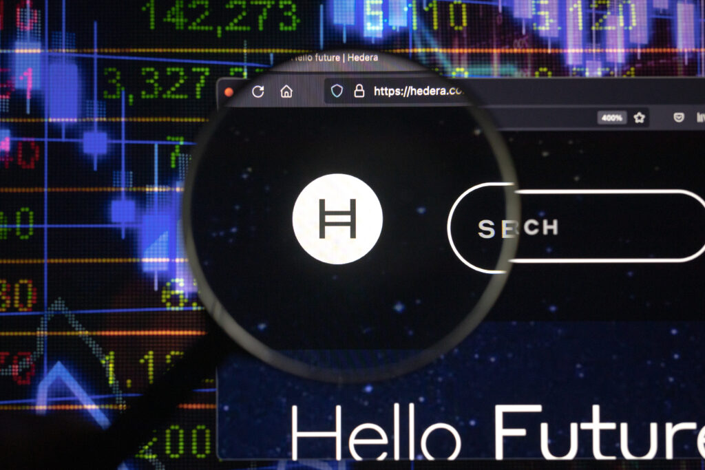 Hedera crypto company logo on a website, seen on a computer screen through a magnifying glass.