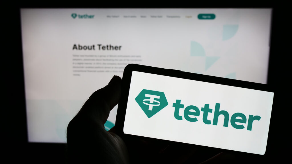 Person holding mobile phone with logo of crypto company Tether Operations Limited on screen in front of business web page.