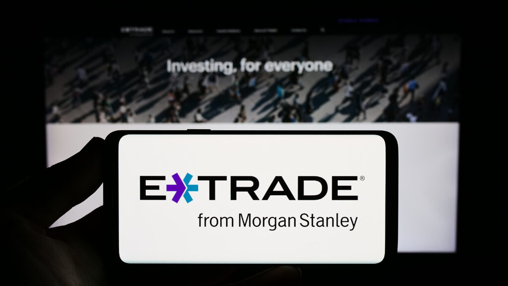 Person holding smartphone with logo of US company E-Trade Financial Corporation on screen in front of website.