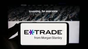 Person holding smartphone with logo of US company E-Trade Financial Corporation on screen in front of website.