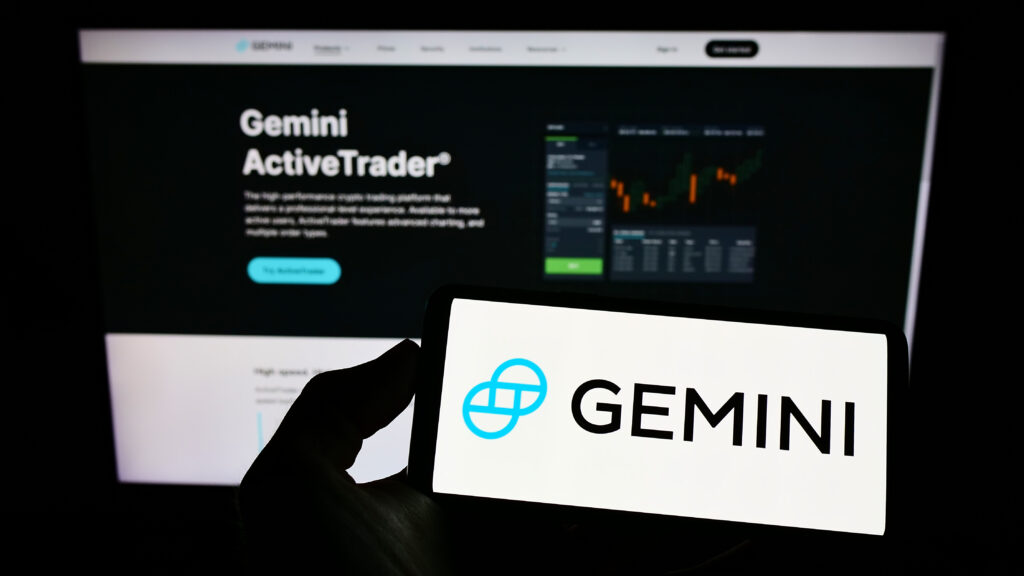 Person holding smartphone with logo of US crypto company Gemini Trust Company LLC on screen in front of website.